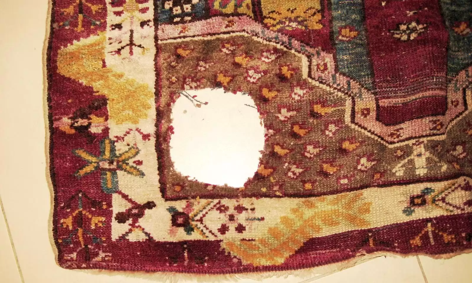 Antique rug with large visible hole before professional restoration