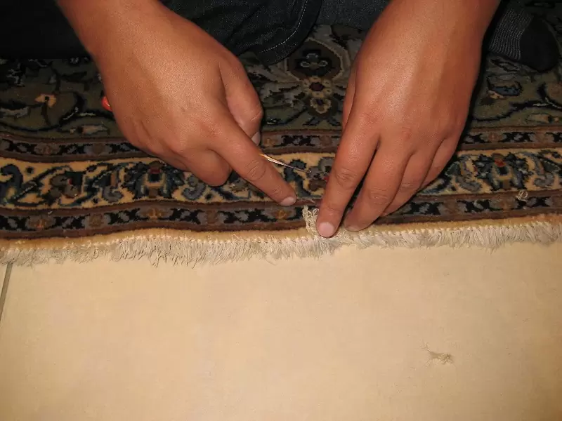 A repairman repairing an antique oriental rug in a restoration workshop.