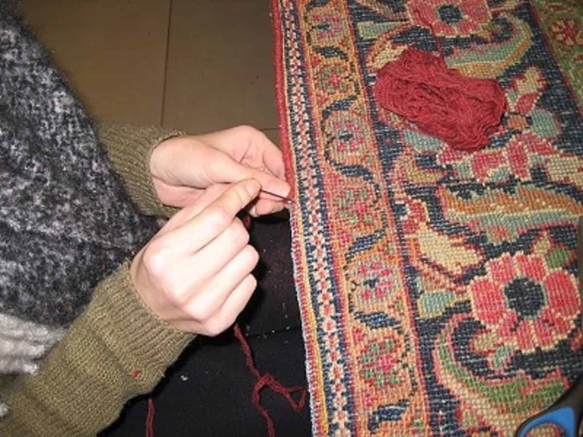 Skilled woman repairing a section of a vibrant, hand-knotted oriental rug with needle and thread.