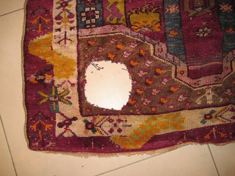 Antique hand-knotted carpet showing significant wear and a large hole, awaiting professional repair.