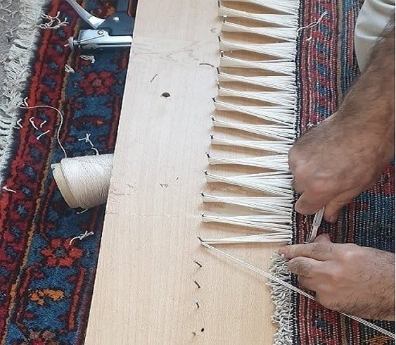Close-up of a repair technician expertly attaching fresh fringes to a vintage rug.