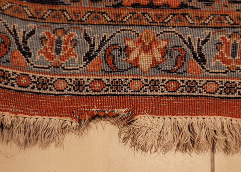 Close-up of a damaged oriental rug with a noticeable hole and missing pile before expert repair.