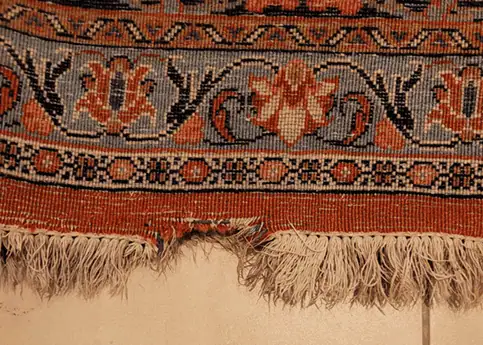 Close-up of a damaged oriental rug with a noticeable hole and missing pile before expert repair.