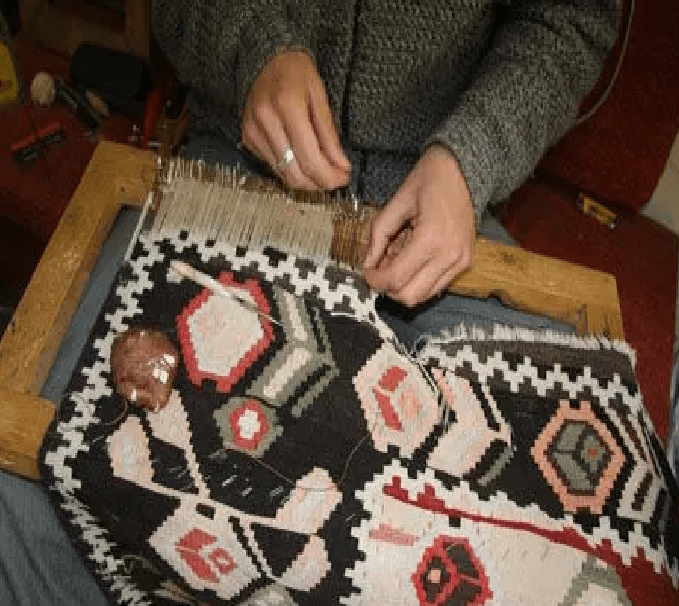 Repairman meticulously repairing an old and worn oriental kilim rug with hand tools.