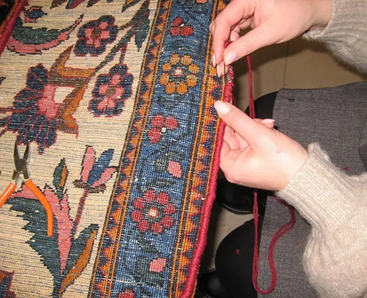 Expert **rug restoration** on a damaged oriental carpet. Repair woman meticulously restores the damaged edge of an oriental rug.