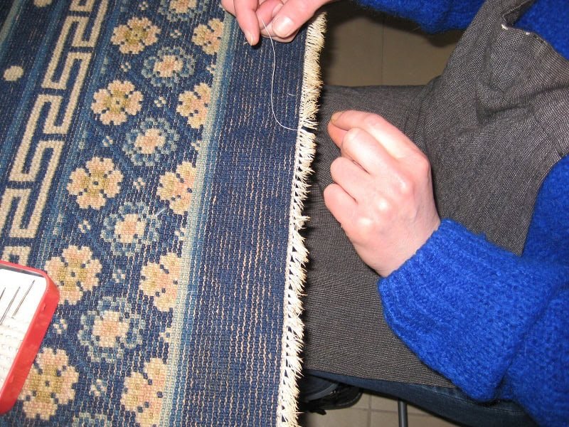 A skilled repair woman meticulously mending the delicate fringes of an ornate oriental rug.