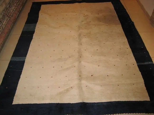 A close-up photo of a handwoven Gabbeh rug from Iran before cleaning, with a large, dark stain on its light-colored wool.